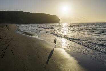 Luftaufnahme einer Frau, die bei Sonnenuntergang am Strand entlang läuft, Praia Areal de Santa Barbara, Ribeira Seca, Azoren, Portugal. - AAEF15160