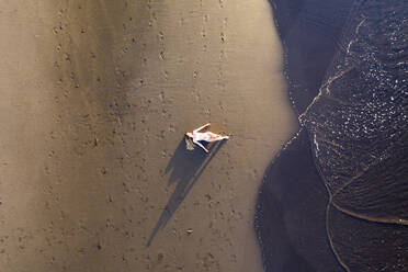 Luftaufnahme einer Frau, die sich bei Sonnenuntergang am Strand entspannt, Praia do Areal de Santa Barbara, Ribeira Seca, Azoren, Portugal. - AAEF15162