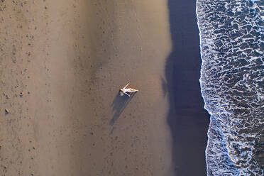 Luftaufnahme einer Frau, die sich bei Sonnenuntergang am Strand entspannt, Praia do Areal de Santa Barbara, Ribeira Seca, Azoren, Portugal. - AAEF15164