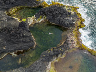 Aerial view of a woman swimming at Mosteiros Rock Pool, Piscinas Naturais Caneiros, Mosteiros, Azores, Portugal. - AAEF15165