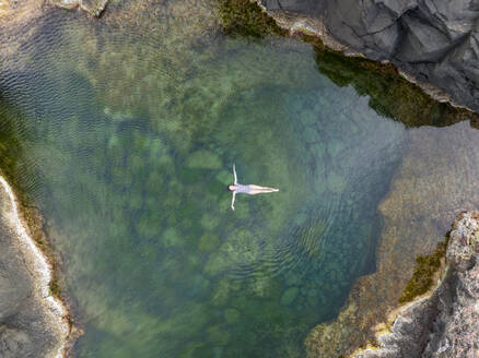 Aerial view of a woman swimming at Mosteiros Rock Pool, Piscinas Naturais Caneiros, Mosteiros, Azores, Portugal. - AAEF15166