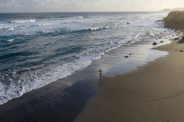 Luftaufnahme einer Frau, die am Strand entlang geht, Praia do Areal de Santa Barbara, Ribeira Seca, Azoren, Portugal. - AAEF15172