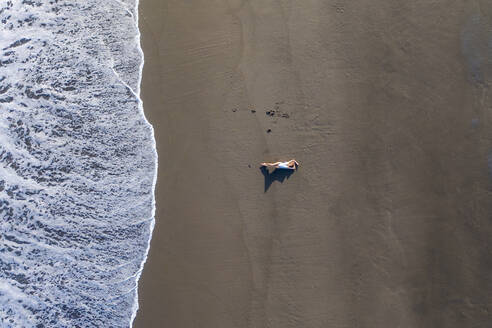 Luftaufnahme einer Frau beim Entspannen am Strand Praia de Areal de Santa Barbara, Ribeira Seca, Azoren, Portugal. - AAEF15174