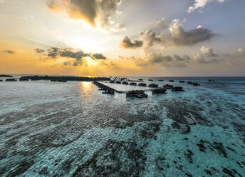 Malediven, Nord-Male-Atoll, Lankanfushi, Luftaufnahme des Indischen Ozeans bei Sonnenuntergang mit Bungalows der Ferienanlage im Hintergrund - AMF09557