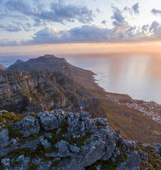 Luftaufnahme von Person über dem Gipfel mit Blick auf die Stadt und den Ozean bei Sonnenuntergang im Naturschutzgebiet Tafelberg, Kapstadt Westkap, Südafrika. - AAEF15210