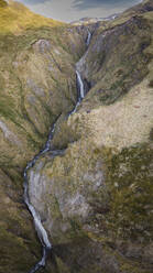 Luftaufnahme eines kleinen Flusses, der an einem Berg auf der Insel Unalaska, Alaska, Vereinigte Staaten, entlangfließt. - AAEF15307