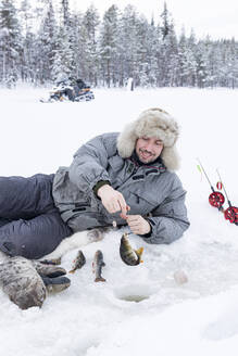 Fröhlicher Mann, der den Fischfang aus dem Eisloch aufnimmt, Lappland, Schweden, Skandinavien, Europa - RHPLF22682