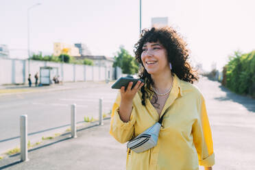 Smiling woman sending voicemail through smart phone on street - MEUF07453