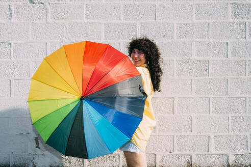 Happy woman spinning multi colored umbrella on sunny day - MEUF07468