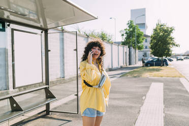 Young woman talking on mobile phone standing at bus stop - MEUF07471