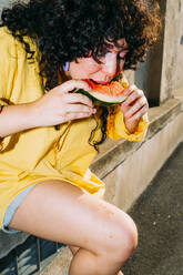 Frau isst Wassermelonenscheibe auf einer Bank sitzend - MEUF07491