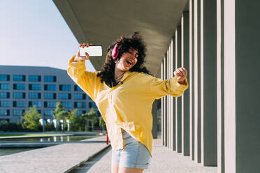 Carefree young woman listening music and dancing by building - MEUF07501