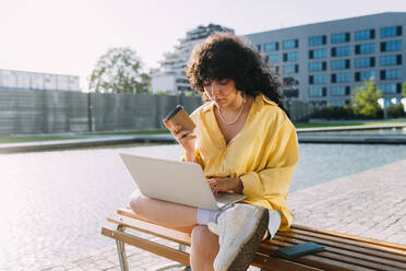 Junge Frau beim E-Learning am Laptop in der Stadt an einem sonnigen Tag - MEUF07504