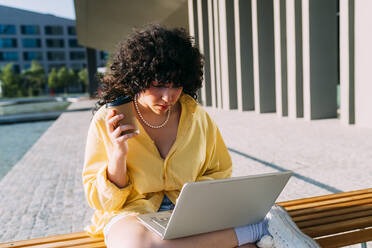 Junge Studentin beim E-Learning am Laptop in der Stadt an einem sonnigen Tag - MEUF07505