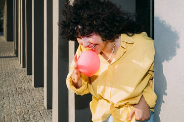 Smiling woman blowing bubble gum by column on sunny day - MEUF07509