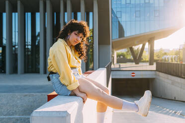 Young woman sitting on bench by building - MEUF07520