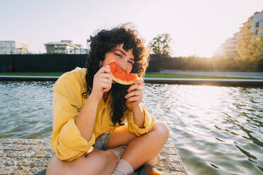 Junge Frau isst Wassermelone am Teich - MEUF07541