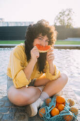 Frau mit Orangen im Netzbeutel isst Wassermelone am Teich - MEUF07543