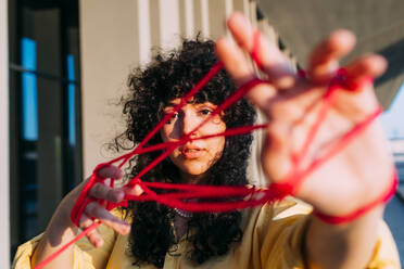 Young woman playing cats cradle with red thread - MEUF07554