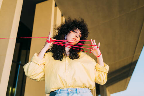 Curly hair woman playing cats cradle with thread - MEUF07557