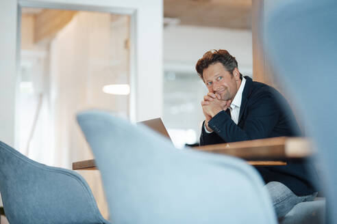 Thoughtful businessman sitting at desk in office - KNSF09582