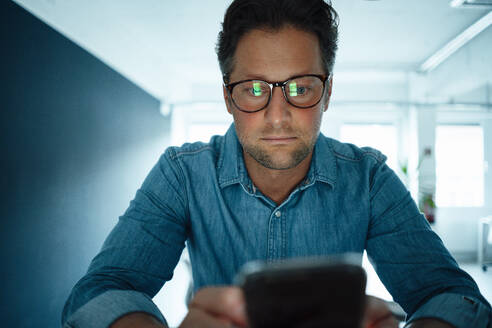 Geschäftsmann mit Brille und Mobiltelefon im Büro - KNSF09595