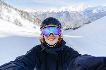 Smiling woman wearing ski goggles front of snow covered mountains - OMIF01044