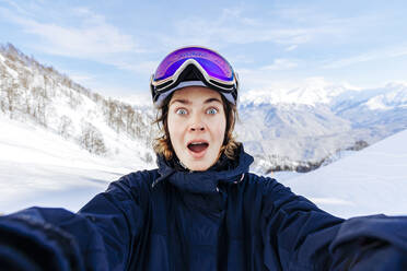 Shocked woman with mouth open in front of snowy mountains - OMIF01045