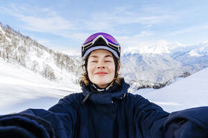 Frau mit geschlossenen Augen genießt vor schneebedeckten Bergen - OMIF01046
