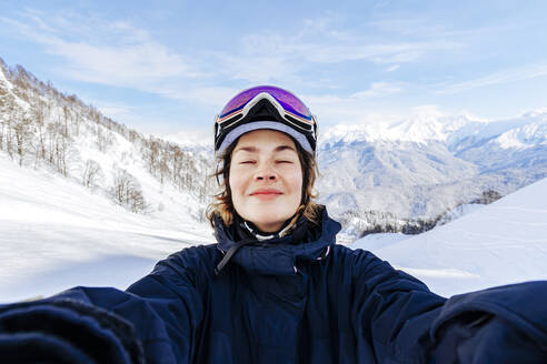 Frau mit geschlossenen Augen genießt vor schneebedeckten Bergen - OMIF01046