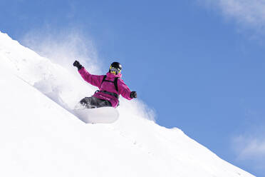 Man with arms outstretched snowboarding on snowy mountains under blue sky - OMIF01056