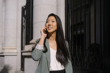 Junge Frau spricht mit einem Smartphone vor einem Gebäude - MMPF00204