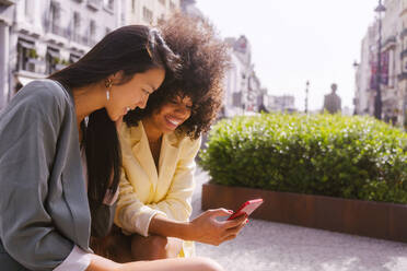 Smiling woman sharing smart phone with friend - MMPF00213