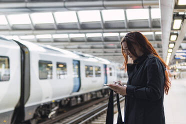 Redhead woman using smart phone at railroad station platform - PNAF04300