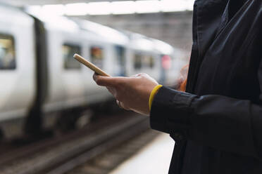 Hands of woman using mobile phone at railroad station platform - PNAF04301