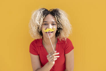 Glückliche Frau mit Schnurrbartstütze vor gelber Wand - JCCMF06864