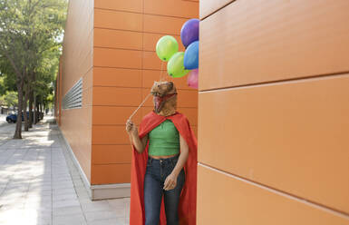 Frau mit Krokodilmaske läuft mit bunten Luftballons vor einer Wand - JCCMF06890