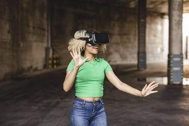 Lächelnde Frau in einem Virtual-Reality-Simulator gestikuliert in einem Parkhaus - JCCMF06903