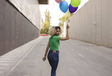 Lächelnde Frau mit buntem Luftballon auf der Straße - JCCMF06906