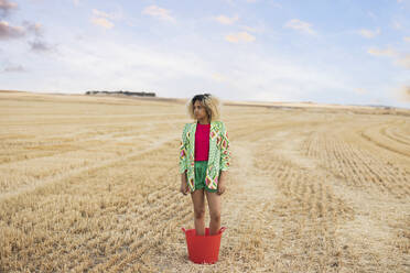 Young woman standing in bucket at field - JCCMF06907