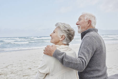 Senior couple standing on the beach with arms around - RORF02977