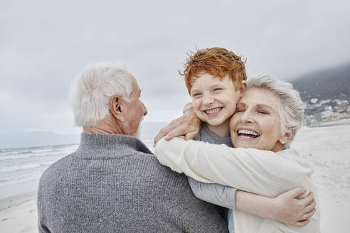 Caring grandparents embracing grandson on the beach - RORF02986