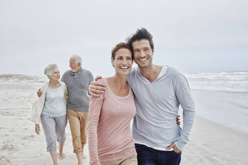 Adult couple walking with senior parents on the beach - RORF02994