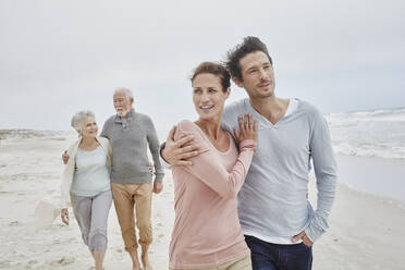 Adult couple walking with senior parents on the beach - RORF02995