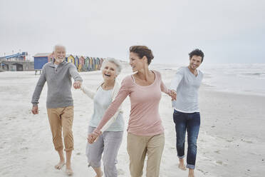 Adult couple walking with senior parents on the beach - RORF02998