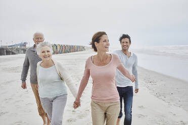 Adult couple walking with senior parents on the beach - RORF02999