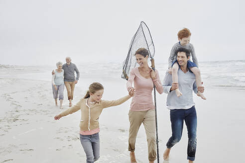 Carefree family with daughter walking on the beach grandparents following in background - RORF03011