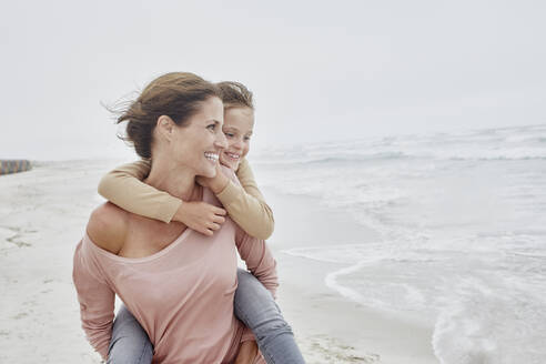 Mutter geht am Strand spazieren und trägt ihre Tochter Huckepack - RORF03016