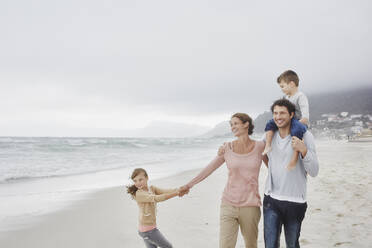 Eltern gehen mit zwei Kindern am Strand spazieren und tragen ihren Sohn auf den Schultern - RORF03037