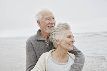 Happy senior couple standing smiling on windy beach - RORF03049